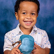 Calvin joined the competition — help win amazing prizes! child, portrait, smiling, happy, curly_hair, teeth, blue_background, studio, photography, fashion, shirt, patterned_clothing, hat, blue_hat, gold_buckle, accessory, holding_object, hands, closeup, indoors