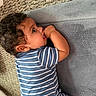 baby, blue_clothing, candid, carpet, chewing, child, couch, curly_hair, face, hand, home, indoor, infant, photography, portrait, relaxed, sitting, smiling, sofa, striped_outfit