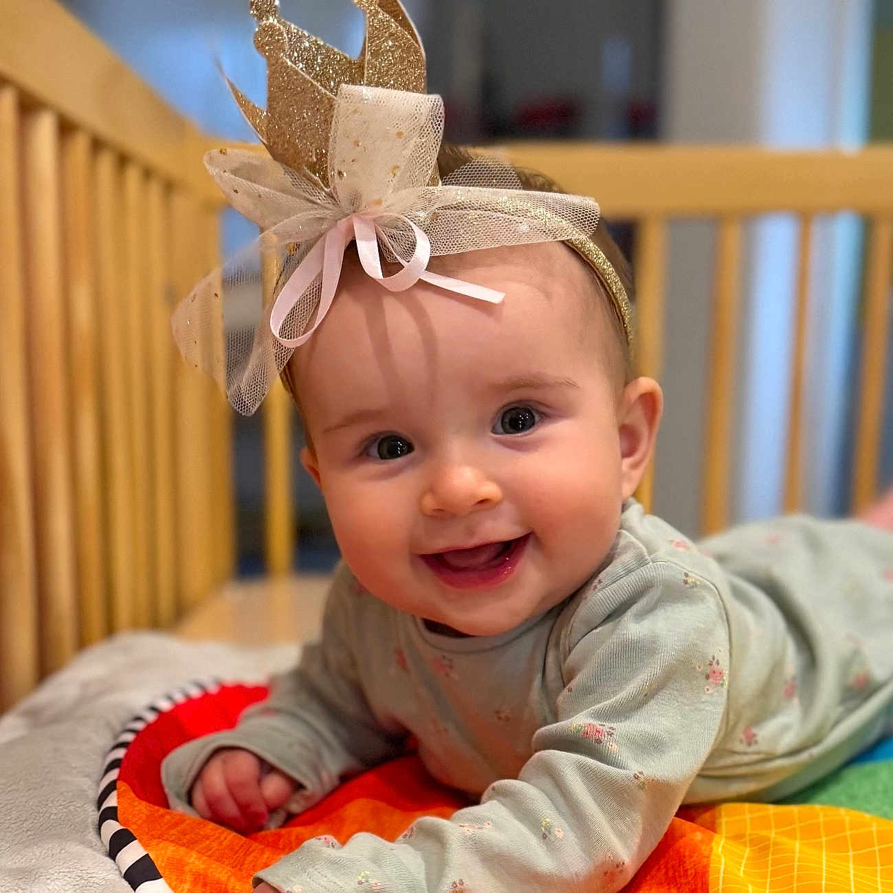 Alyssa is registered to the contest to win money with this photo: baby, blanket, child, clothing, colorful, cozy, crib, crown, cute, face, happy, headband, indoor, infant, person, playtime, portrait, smiling, soft, toddler