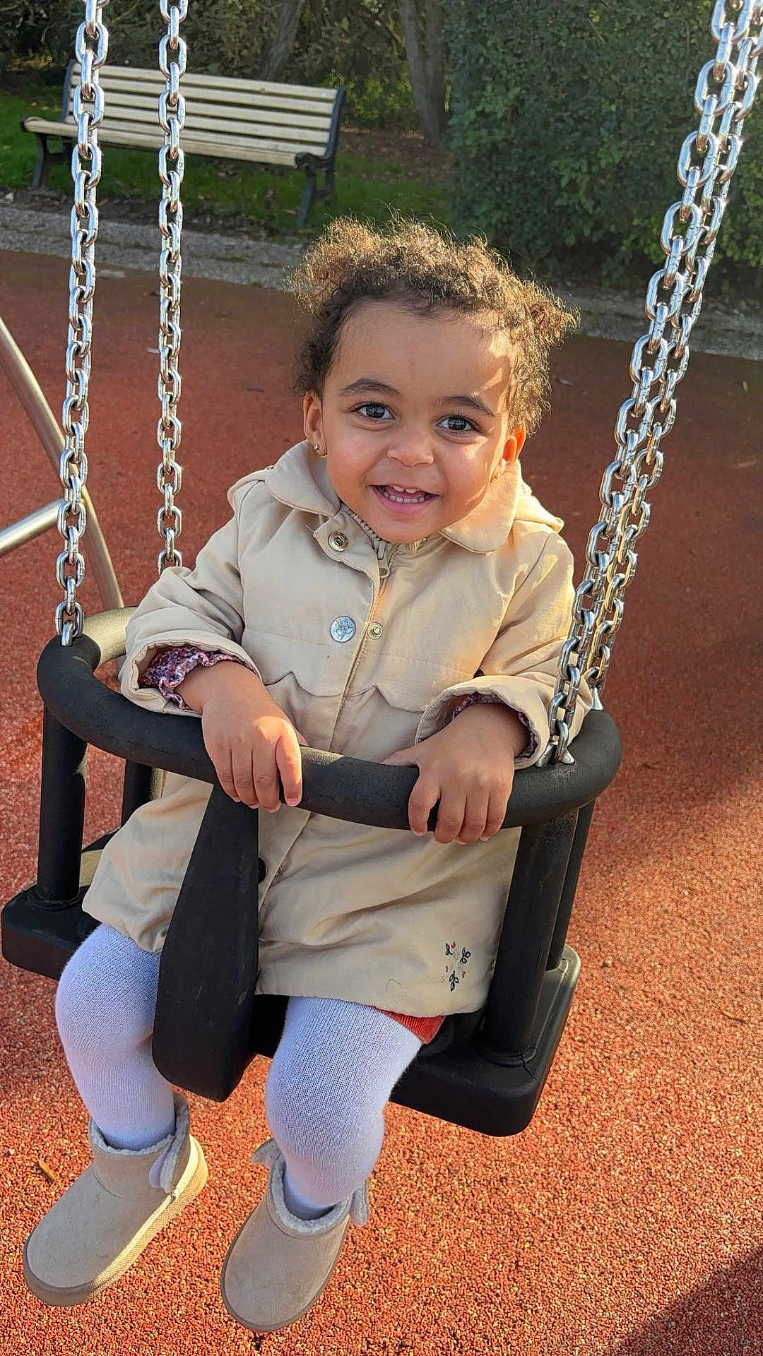 Akia a rejoint le concours — aidez-le/la à gagner de superbes lots ! toddler, child, swing, playground, smiling, outdoor, park, bench, chains, jacket, curly_hair, happy, person, footwear, grass, sunlight, toy, seat, autumn, casual_clothing