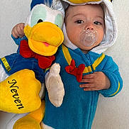 Neven participe au concours pour gagner de l'argent avec cette photo : baby, blue, child, costume, cute, donald_duck, face, hand, hood, indoor, infant, pacifier, person, plush_toy, portrait, red, smile, soft_toy, white, yellow