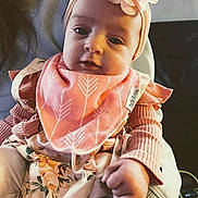 Brittney joined the competition — help win amazing prizes! baby, child, headband, flower, pink_clothing, bib, hand, person, indoor, soft_lighting, portrait, cute, infant, holding, sweater, patterned_clothing, closeup, face, young_child, adorable