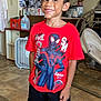 child, boy, smiling, red_tshirt, spiderman, shorts, indoor, kitchen, floor, rug, cabinet, fan, baby_chair, person, happy, standing, clothing, toy, home, portrait