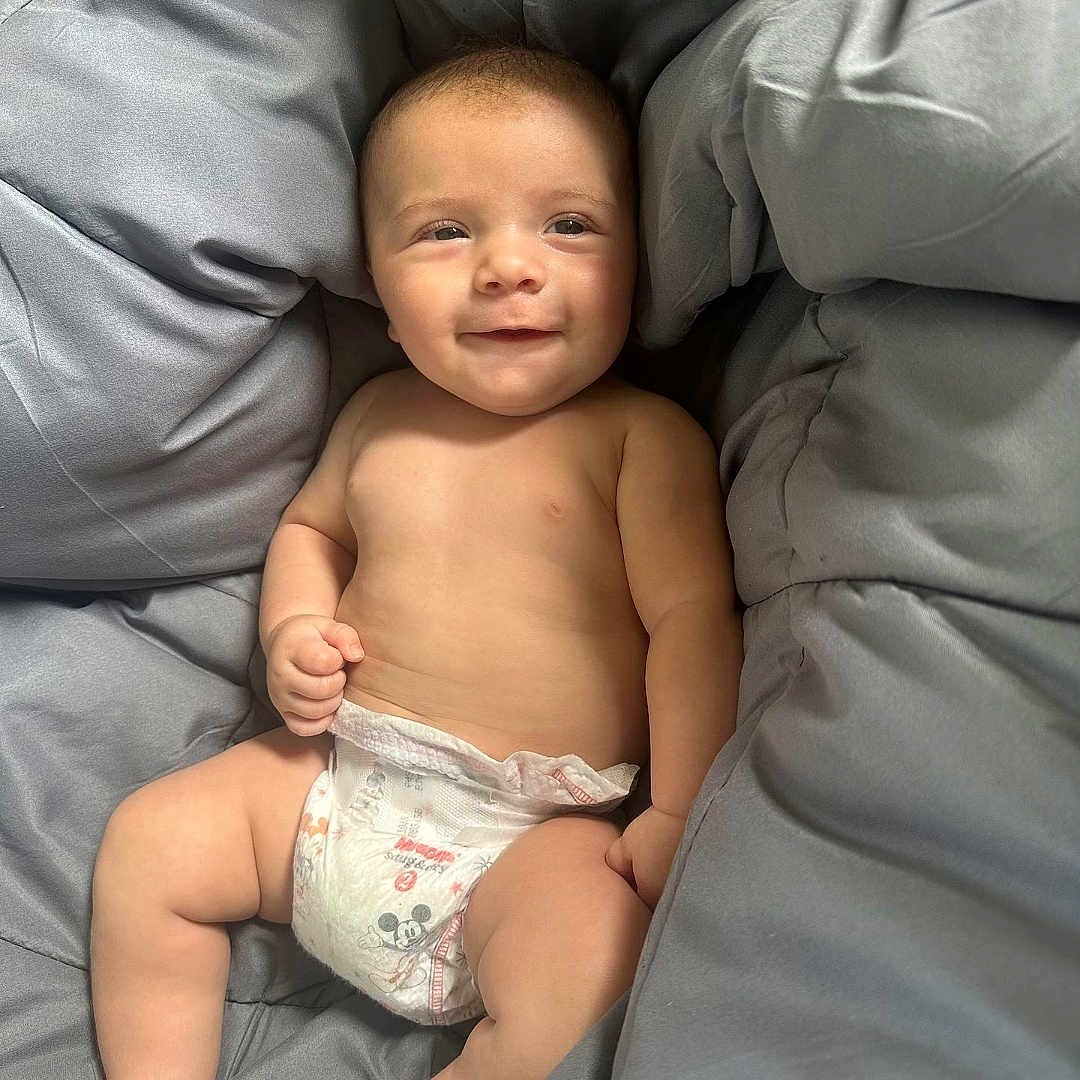 Carson joined the competition — help win amazing prizes! baby, bare_chest, blanket, child, comfort, cute, diaper, gray, happy, indoors, infant, lying_down, mickey_mouse, person, plush, relaxing, skin, smile, soft, young