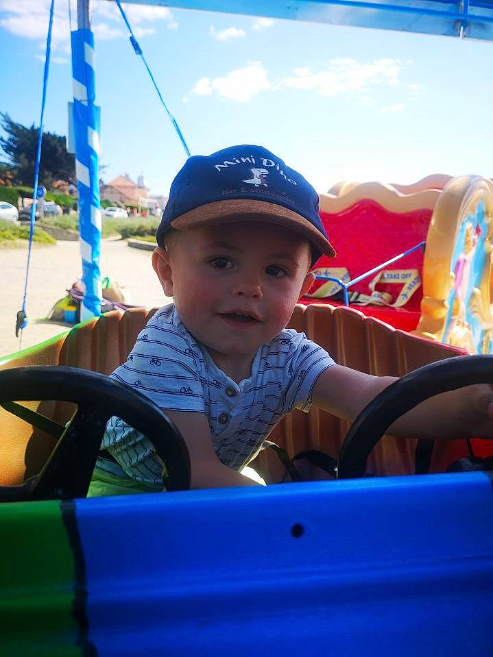 Lewis a rejoint le concours — aidez-le/la à gagner de superbes lots ! automotive_exterior, baseball_cap, blue, cap, child, city, cloud, electric_blue, fun, happy, hat, headwear, leisure, motor_vehicle, nonbuilding_structure, person, recreation, sitting, sky, toddler