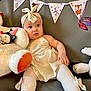 baby, child, dress, headband, soft_toys, stuffed_animal, couch, decorations, banner, butterfly, white_tights, ribbon, celebration, indoor, portrait, cute, milestone, infant, happy, cozy