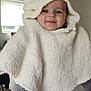 baby, child, hooded_poncho, white_clothing, smiling, blue_eyes, person_holding, gray_sweater, indoor, home_interior, window, natural_light, cute, warm_clothing, portrait, happy, infant, soft_texture, cozy, baby_fashion