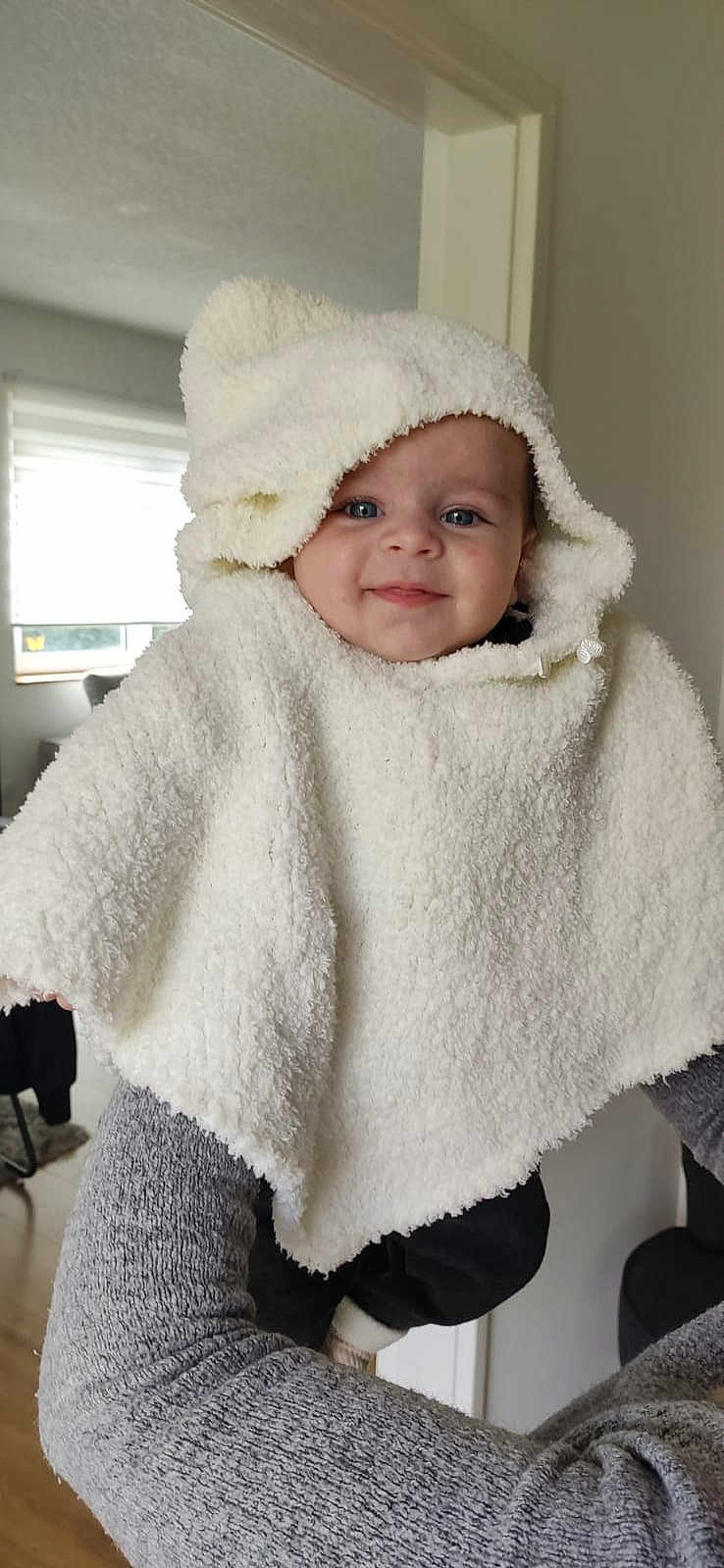 Thibault participe au concours pour gagner de l'argent avec cette photo : baby, child, hooded_poncho, white_clothing, smiling, blue_eyes, person_holding, gray_sweater, indoor, home_interior, window, natural_light, cute, warm_clothing, portrait, happy, infant, soft_texture, cozy, baby_fashion