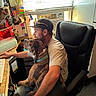 Tyson is registered to the contest to win money with this photo: man, dog, office_chair, computer, desk, window_blinds, sunglasses, cap, collar, workspace, keyboard, air_conditioner, papers, shelf, pen_holder, light, electronics, carpet, person, indoor