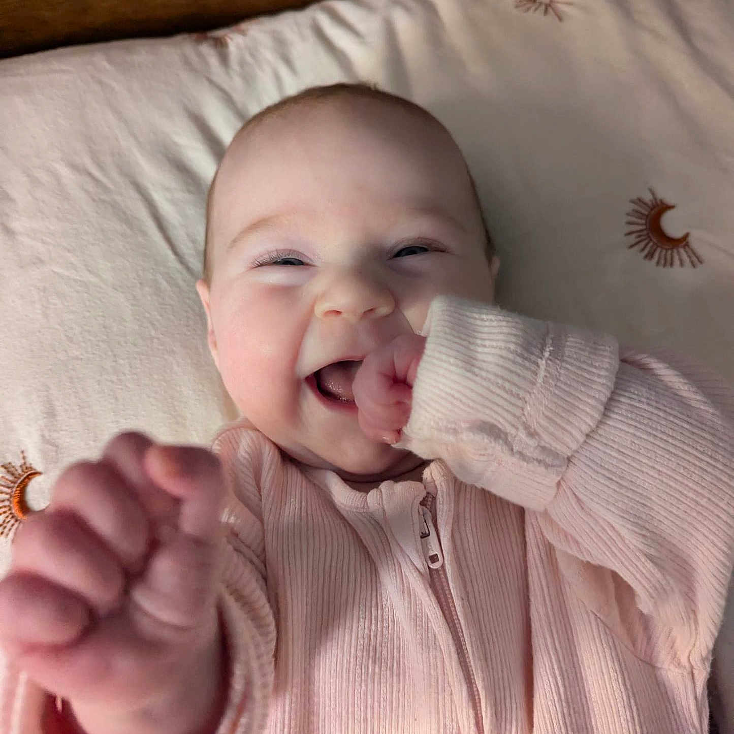Daphne is registered to the contest to win money with this photo: baby, bed, bedding, child, clothing, cozy, cute, face, hand, happy, infant, lying_down, moon, pattern, pink, portrait, smiling, soft, sun, young
