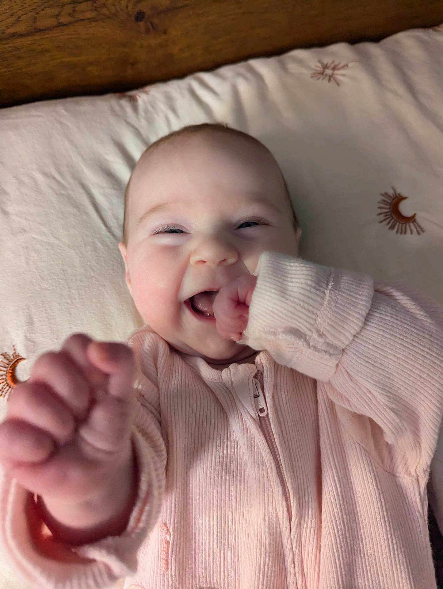 Daphne is registered to the contest to win money with this photo: baby, infant, smiling, happy, hand, clothing, pink, bed, bedding, moon, sun, pattern, face, cute, child, portrait, young, lying_down, soft, cozy