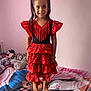 child, girl, dress, red_dress, polka_dot, ruffles, barefoot, bed, bedspread, stuffed_animals, pink_wall, smiling, long_hair, pigtails, indoor, portrait, happy, clothing, toy, room