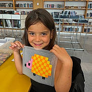 Layana a rejoint le concours — aidez-le/la à gagner de superbes lots ! child, girl, smiling, pixel_art, turtle, craft, library, bookshelf, table, chair, indoors, art, colorful, happy, person, play, plastic_board, long_hair, black_clothing, education