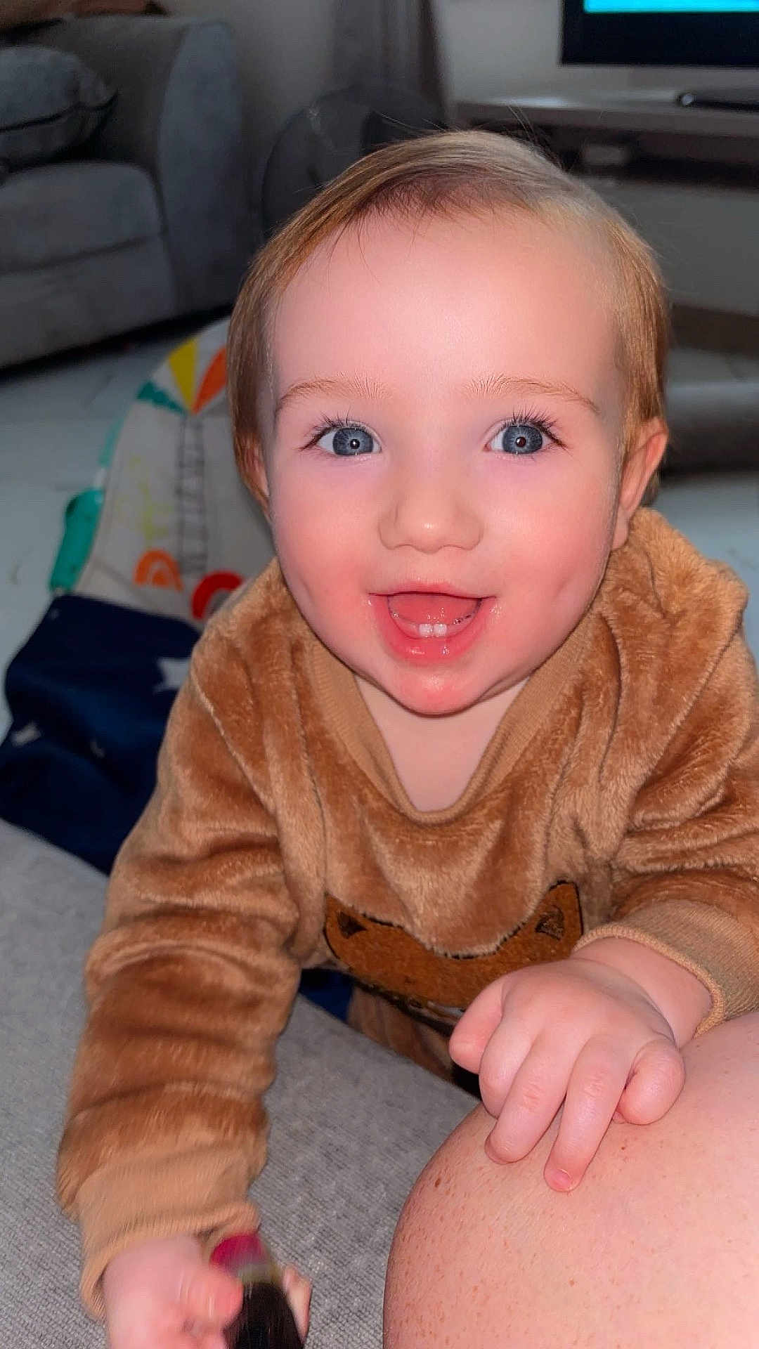 Austin-James is registered to the contest to win money with this photo: toddler, child, smiling, face, blue_eyes, sweater, fuzzy_clothing, hand, indoor, living_room, sofa, couch, toy, happy, person, closeup, baby, cute, skin, expression