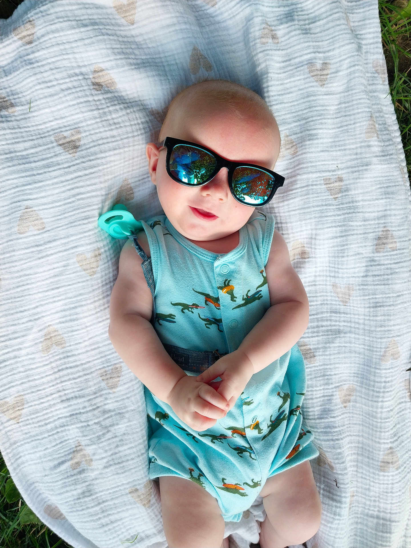 Asher is registered to the contest to win money with this photo: baby, sunglasses, blanket, outdoor, grass, infant, onesie, dinosaur_pattern, reflection, hands, cute, child, casual, sunny, relaxing, portrait, young, wearing, fashion, summer