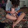 Raven is registered to the contest to win money with this photo: baby, bed, bedroom, blanket, blue_shorts, camouflage, caregiver, child, family, gray_shirt, holding, home, indoor, infant, person, phone, portrait, sitting, sleeping, smartphone
