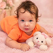 Sophía joined the competition — help win amazing prizes! baby, child, infant, portrait, smiling, wide_eyed, orange_outfit, curly_hair, brown_hair, earrings, plush_toy, bunny, stuffed_animal, pink_blanket, fuzzy_blanket, lying_down, indoor, close_up, adorable, nursery