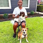 Buster joined the competition — help win amazing prizes! man, dog, pet, grass, yard, house, window, flag, leash, sitting, outdoor, shoes, shorts, white_shirt, fence, shrub, daylight, smiling, chair, portrait
