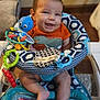 baby, smiling, infant, baby_seat, toy, indoor, colorful, orange_shirt, dinosaur_print, feet, face, happy, child, window_blinds, cushion, plastic_toy, playful, person, sitting, cute