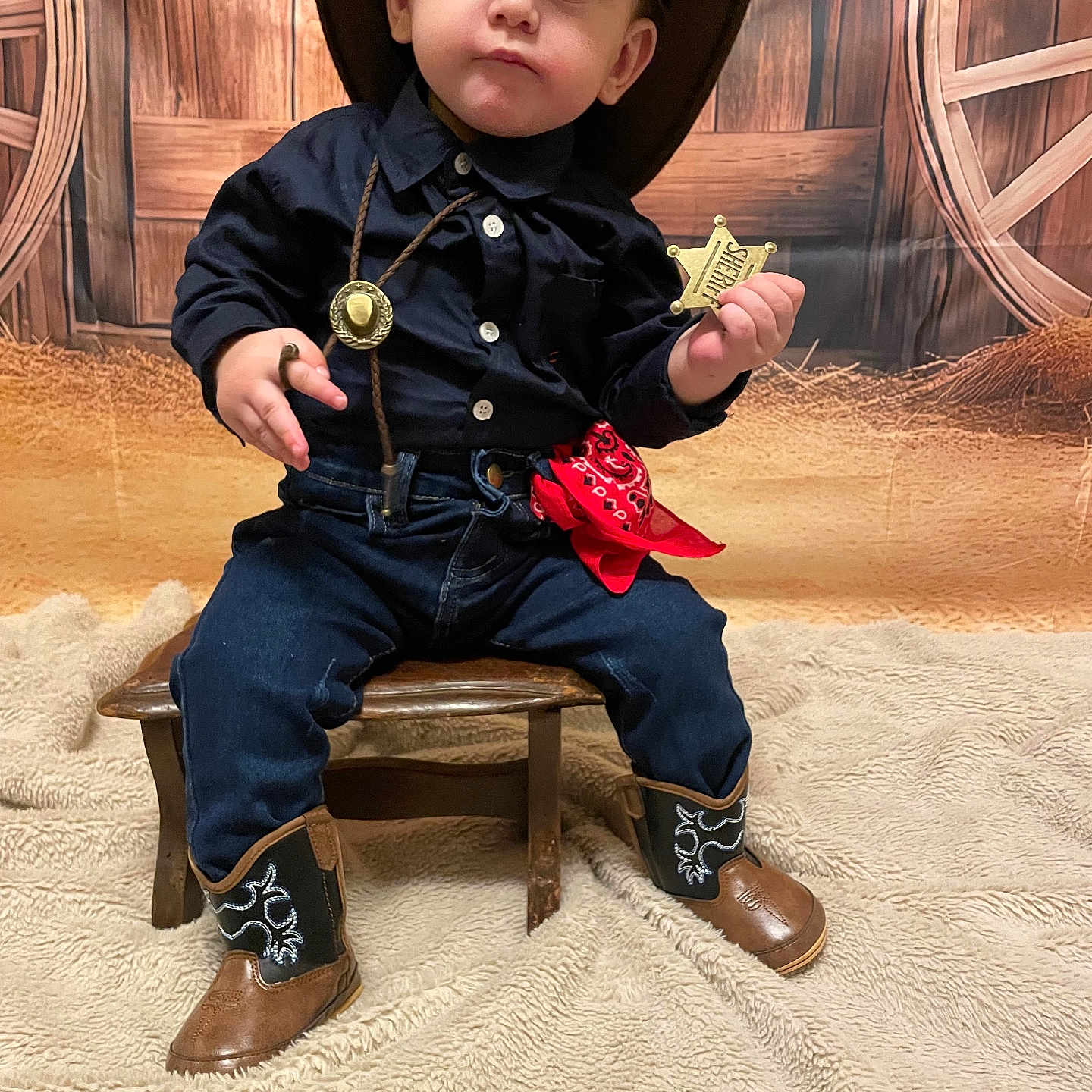 Ezechiel a rejoint le concours — aidez-le/la à gagner de superbes lots ! adorable, blanket, child, cowboy_boots, cowboy_costume, cowboy_hat, cute_expression, hay, indoor, jeans, navy_shirt, photoshoot, portrait, red_bandana, sheriff_badge, sitting, toddler, wagon_wheel, western_backdrop, wooden_stool