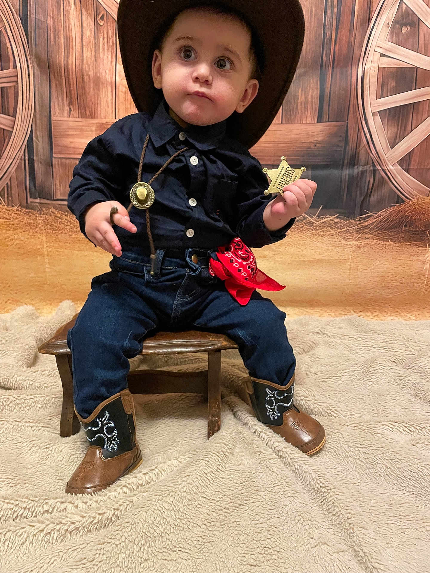 Ezechiel a rejoint le concours — aidez-le/la à gagner de superbes lots ! child, toddler, cowboy_costume, cowboy_hat, sheriff_badge, red_bandana, cowboy_boots, jeans, navy_shirt, wooden_stool, western_backdrop, wagon_wheel, hay, blanket, portrait, sitting, indoor, adorable, cute_expression, photoshoot