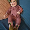 Winter is registered to the contest to win money with this photo: baby, infant, smiling, onesie, boots, headwrap, pillow, blanket, blue, pink, green, happy, cute, child, indoor, portrait, clothing, sitting, cozy, expression