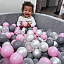 toddler, child, ball_pit, pink_balls, grey_balls, white_balls, curly_hair, smiling, indoor, playtime, happy, soft_furniture, floor_tiles, clothing, person, baby, fun, toy, home, portrait