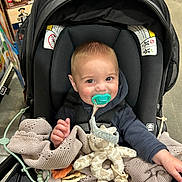Caden is registered to the contest to win money with this photo: baby, pacifier, stroller, blanket, plush_toy, giraffe_toy, smiling, child, indoor, shopping_aisle, person, clothing, seat, happy, cute, infant, baby_toy, knitted_blanket, holding, retail