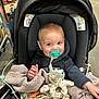baby, pacifier, stroller, blanket, plush_toy, giraffe_toy, smiling, child, indoor, shopping_aisle, person, clothing, seat, happy, cute, infant, baby_toy, knitted_blanket, holding, retail