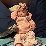 Royalty is registered to the contest to win money with this photo: baby, infant, child, pink_clothing, headband, bow, pillow, blanket, bed, cute, soft_toys, indoor, portrait, sitting, cozy, young_child, face, expression, sleepwear, comfort