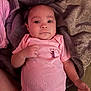 Royalty is registered to the contest to win money with this photo: baby, infant, onesie, pink_clothing, blanket, cozy, lying_down, face, expression, indoors, child, skin, hand, portrait, cute, newborn, person, soft_texture, relaxation, comfort