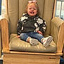 toddler, child, smiling, sitting, chair, wooden_chair, hoodie, jeans, pink_bow, indoor, happy, footwear, sneakers, person, cute, young_child, casual_clothing, furniture, portrait, playful