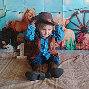 Romeo is registered to the contest to win money with this photo: child, baby, cowboy, hat, vest, boots, blanket, birthday, number_one, western_theme, horses, wagon_wheel, cactus, decorations, indoor, portrait, cute, celebration, smiling, sitting