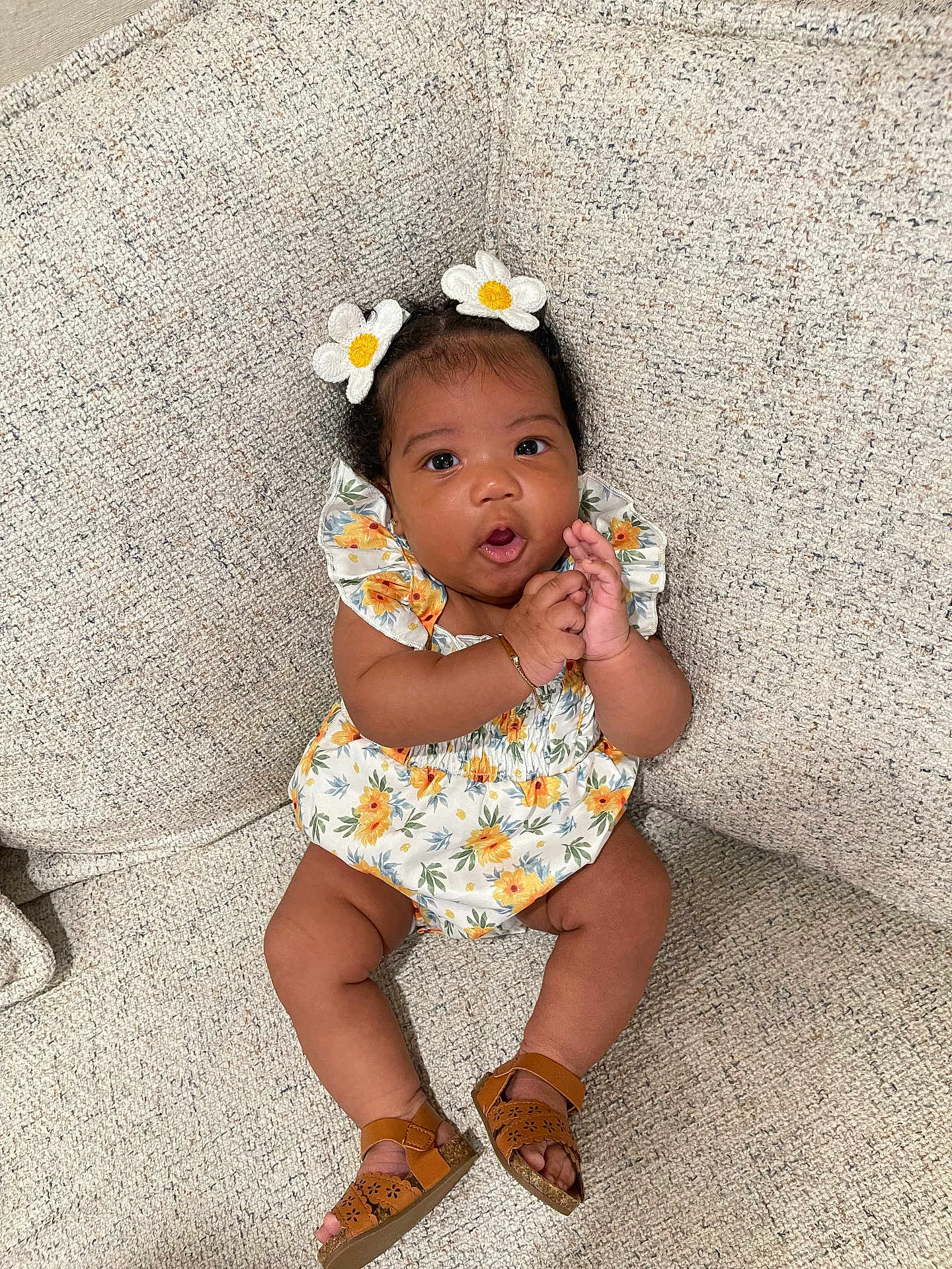 Oaklynn joined the competition — help win amazing prizes! baby, child, girl, flower_hairclip, sitting, couch, floral_dress, sandals, clapping, expression, indoors, cute, happy, person, skin, hand, footwear, texture, comfortable, portrait