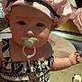 Lilith is registered to the contest to win money with this photo: accessory, baby, bow, carpet, child, clothing, cute, dress, expression, face, hand, hat, indoor, infant, pacifier, pattern, person, sitting, strip, toy