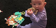 Lilith is registered to the contest to win money with this photo: baby, onesie, toy, carpet, book, walker, floor, indoor, child, infant, purple_clothing, sitting, chewing, play, colorful, soft_toys, home, furniture, person, cute