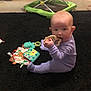 baby, onesie, toy, carpet, book, walker, floor, indoor, child, infant, purple_clothing, sitting, chewing, play, colorful, soft_toys, home, furniture, person, cute
