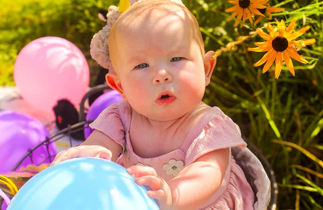 Lilith is registered to the contest to win money with this photo: baby, balloon, pink_dress, flowers, yellow_flowers, garden, outdoor, sunlight, child, curious, face, hand, colorful, nature, greenery, summer, portrait, soft_light, playful, infant