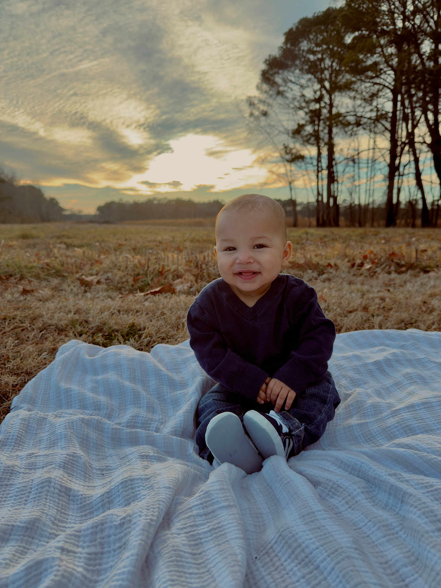 Suede is registered to the contest to win money with this photo: baby, infant, toddler, blanket, outdoor, field, sunset, sky, clouds, trees, grass, smile, portrait, shoes, denim, sweater, sitting, nature, happy, cute