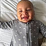 Suede is registered to the contest to win money with this photo: baby, infant, smile, onesie, bed, blanket, pillow, face, cheeks, eyes, mouth, drool, happy, lying_down, cozy, soft_texture, patterned_clothing, indoor, portrait, skin