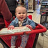 baby, shopping_cart, store, child, tongue_out, denim_jacket, floral_pants, playful, indoor, person, floor_tiles, shopping, people, casual_clothing, footwear, retail, smiling, cute, red, fun