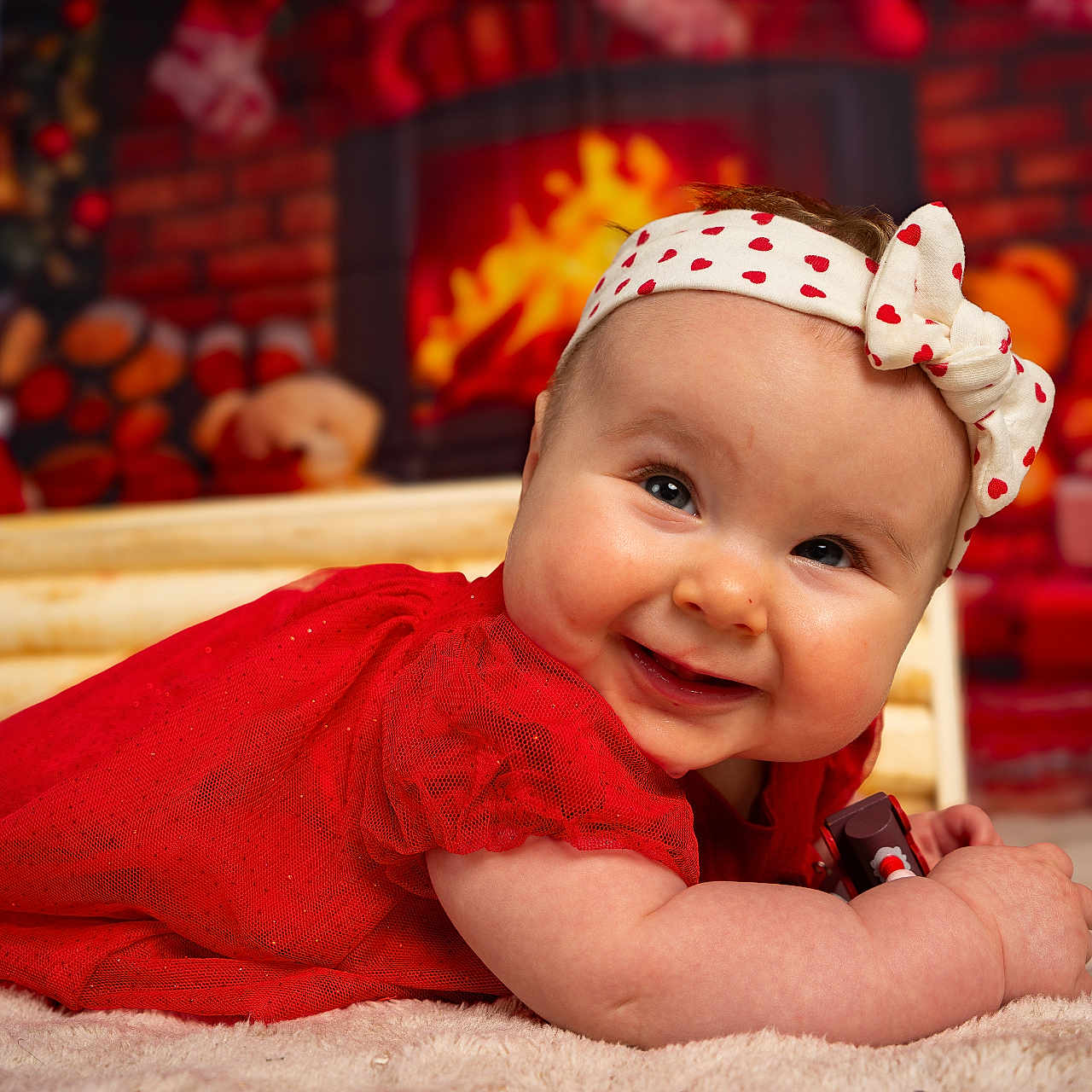 Ella participe au concours pour gagner de l'argent avec cette photo : baby, child, red_dress, headband, smile, carpet, fireplace, christmas, holiday, decorations, stuffed_animals, warm_lighting, indoor, portrait, cute, happy, infant, toy, festive, cozy