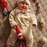 baby, infant, smiling, knitwear, red_hat, plush_toy, elf_doll, carpet, holiday_decor, christmas_theme, ornaments, cozy, cute, indoors, child, festive, soft_texture, toy, cheerful, winter_clothing