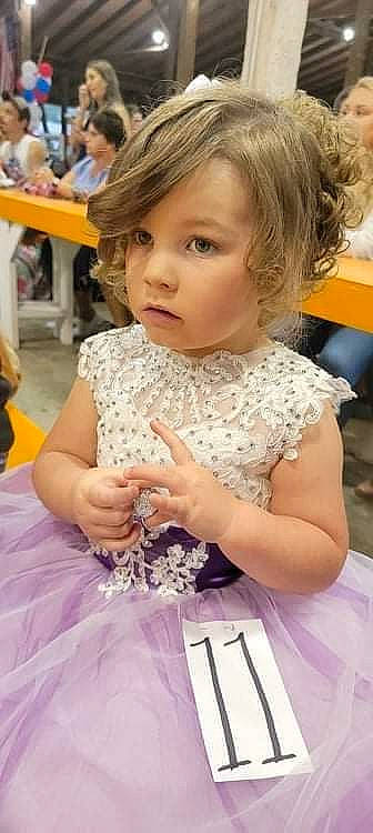 Ridley joined the competition — help win amazing prizes! blurred, bridal_clothing, chair, child, dress, event, finger, formal_wear, fun, gown, hairstyle, happy, head, iris, person, sitting, skin, table, toddler, tradition