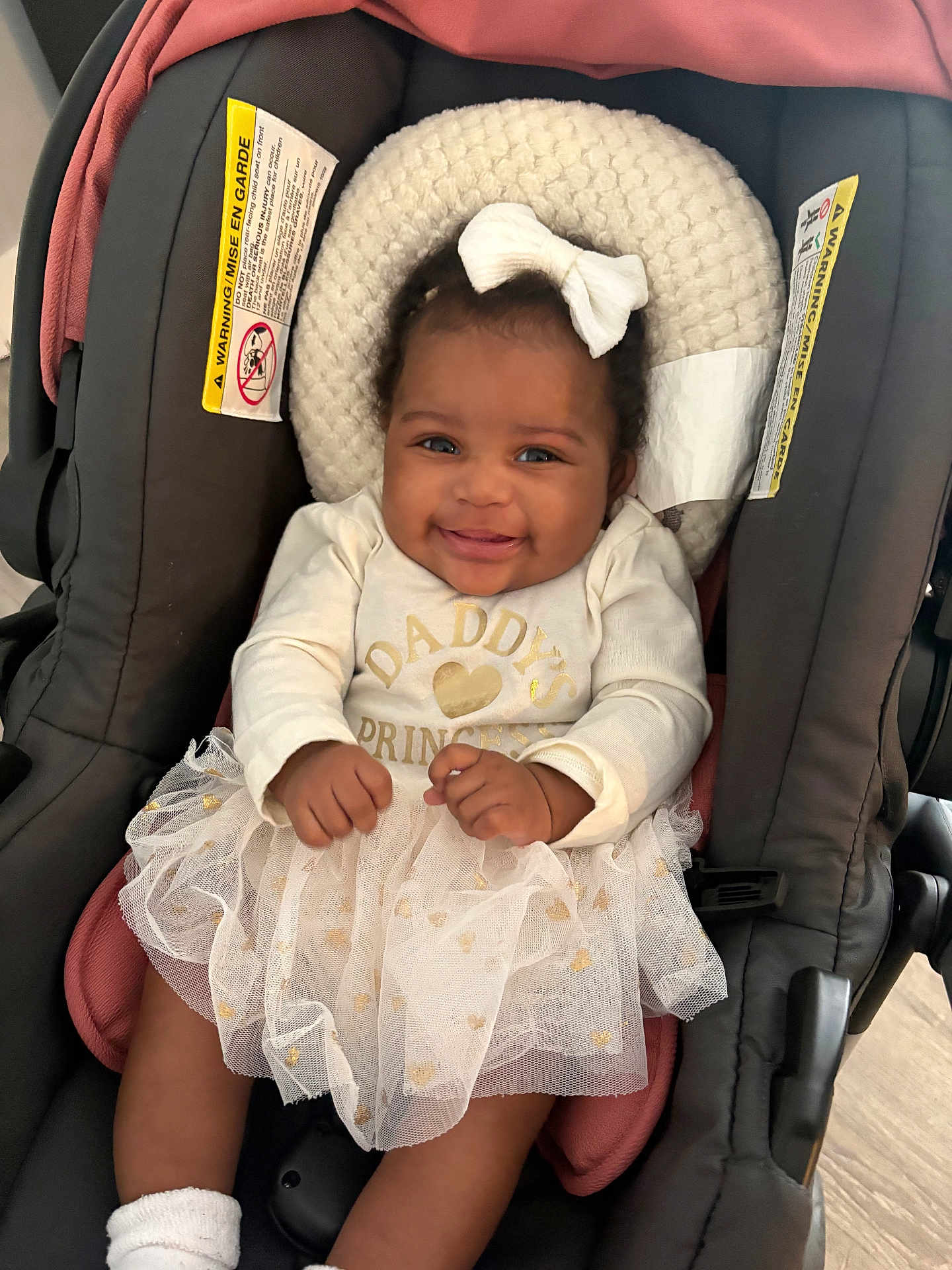 Milani is registered to the contest to win money with this photo: baby, infant, child, car_seat, smile, white_clothing, bow, tutu, cute, happy, indoors, seat, young_child, portrait, person, fashion, apparel, footwear, sock, closeup