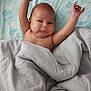 baby, infant, blanket, bed, bedding, arms_up, face, skin, expression, cozy, lying_down, head, comfort, patterned_bedspread, sleepwear, indoors, cute, child, person, resting