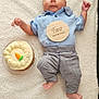 baby, infant, two_months, blue_shirt, striped_pants, carrot_cake, wooden_plaque, blanket, cute, celebration, milestone, lying_down, cheeks, hands, feet, portrait, smiling, indoors, soft_texture, clothing
