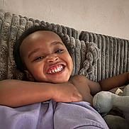 Ahmir is registered to the contest to win money with this photo: child, toddler, smile, happy, couch, blanket, plush, indoor, face, arm, skin, clothing, furniture, cozy, texture, relaxing, cute, portrait, baby, expression