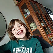 Ethan participe au concours pour gagner de l'argent avec cette photo : child, smiling, indoor, cabinet, wooden_furniture, mirror, green_sweatshirt, missing_teeth, happy, person, portrait, casual_clothing, home, hair, face, seated, light, window, candid, joyful