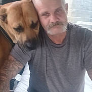 Buddy joined the competition — help win amazing prizes! man, dog, pet, affection, tattoo, casual, indoor, closeup, companion, friendship, head, shoulder, gray_shirt, facial_hair, blurry, portrait, seated, light, window, comfort